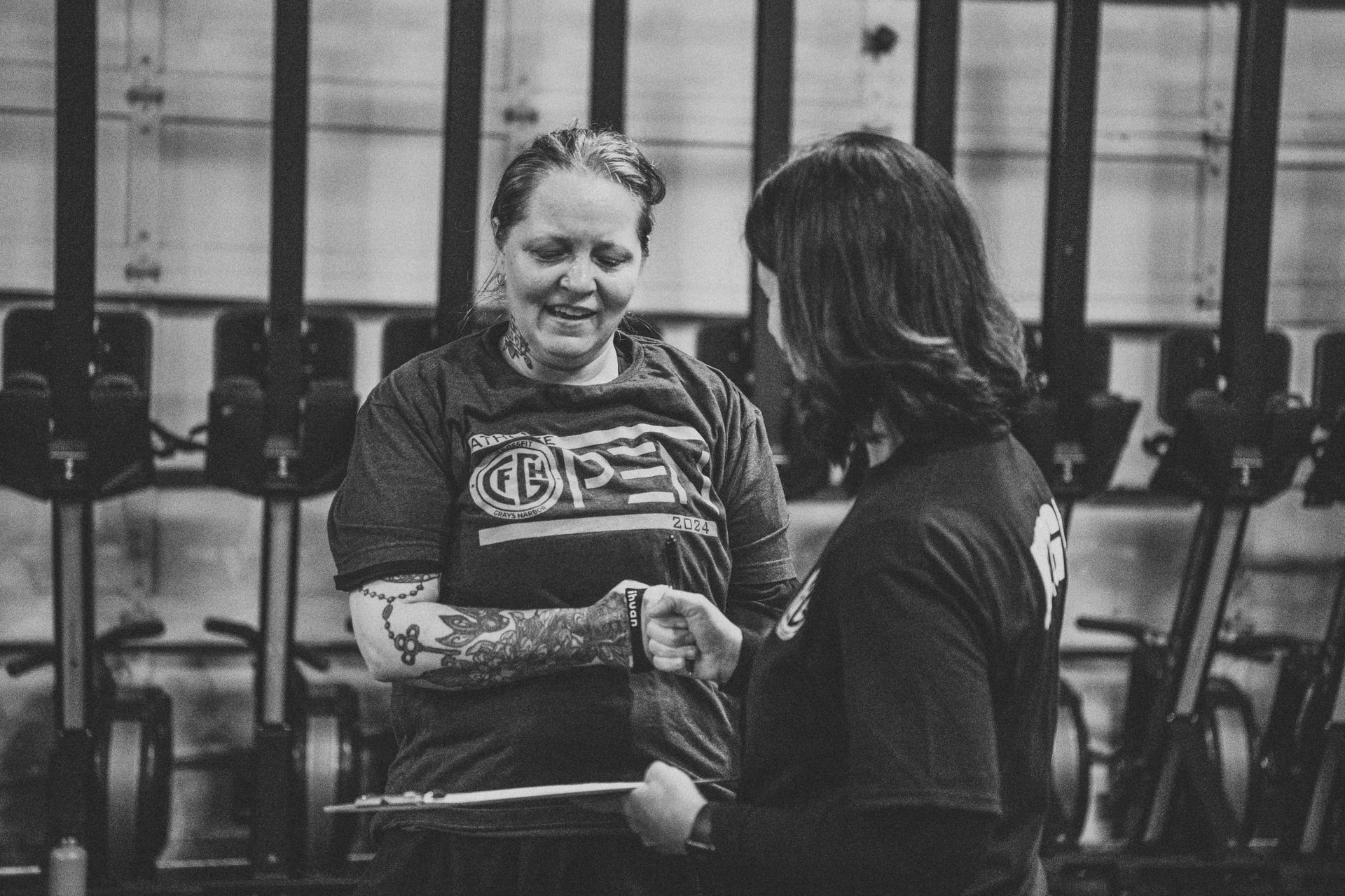 Two women are shaking hands in a gym in a black and white photo.
