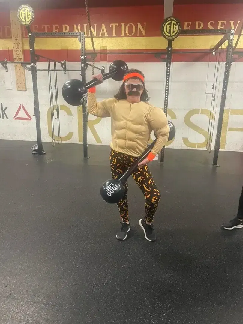 A man in a muscle suit is holding a barbell in a gym.