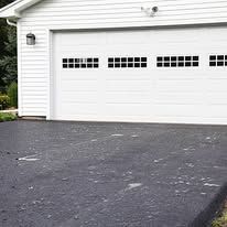 A white garage with a black driveway in front of it.