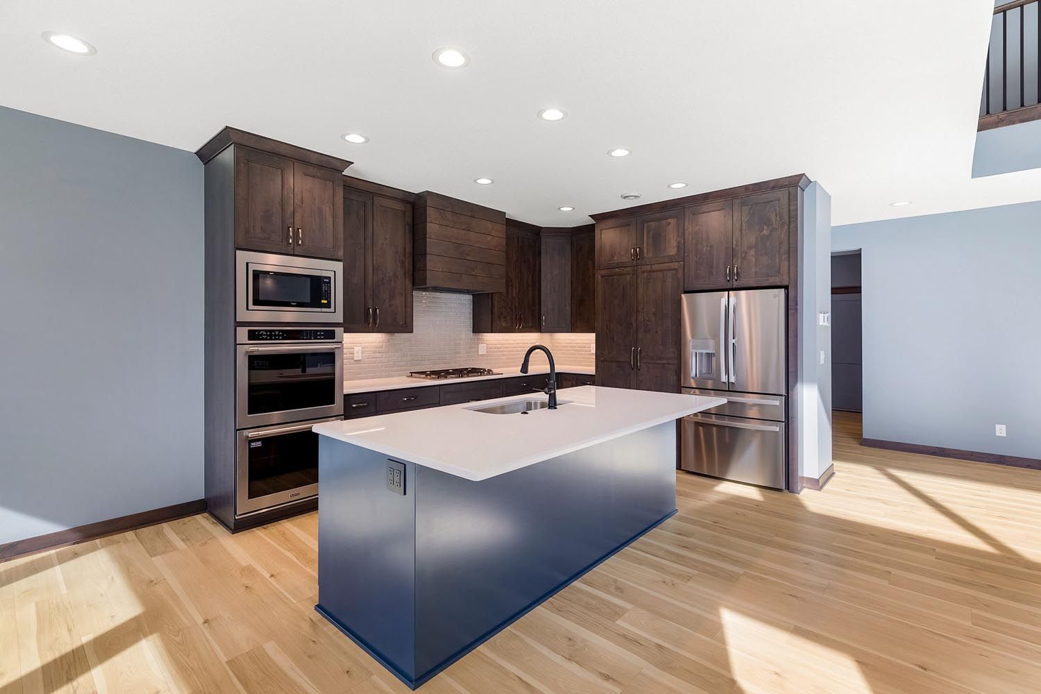 Modern kitchen with dark cabinetry, stainless steel appliances, white countertops, and blue island.