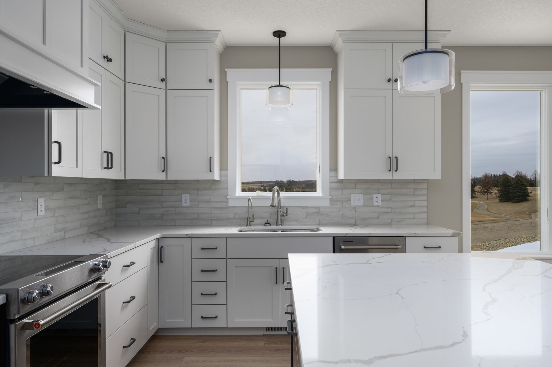 Bright white kitchen with cabinets, countertops, and an island. Stainless steel appliances and a window view.
