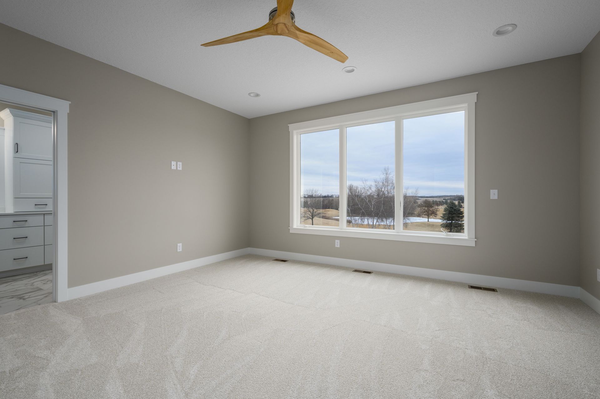 Empty bedroom with neutral walls, carpet, large window, and ceiling fan.