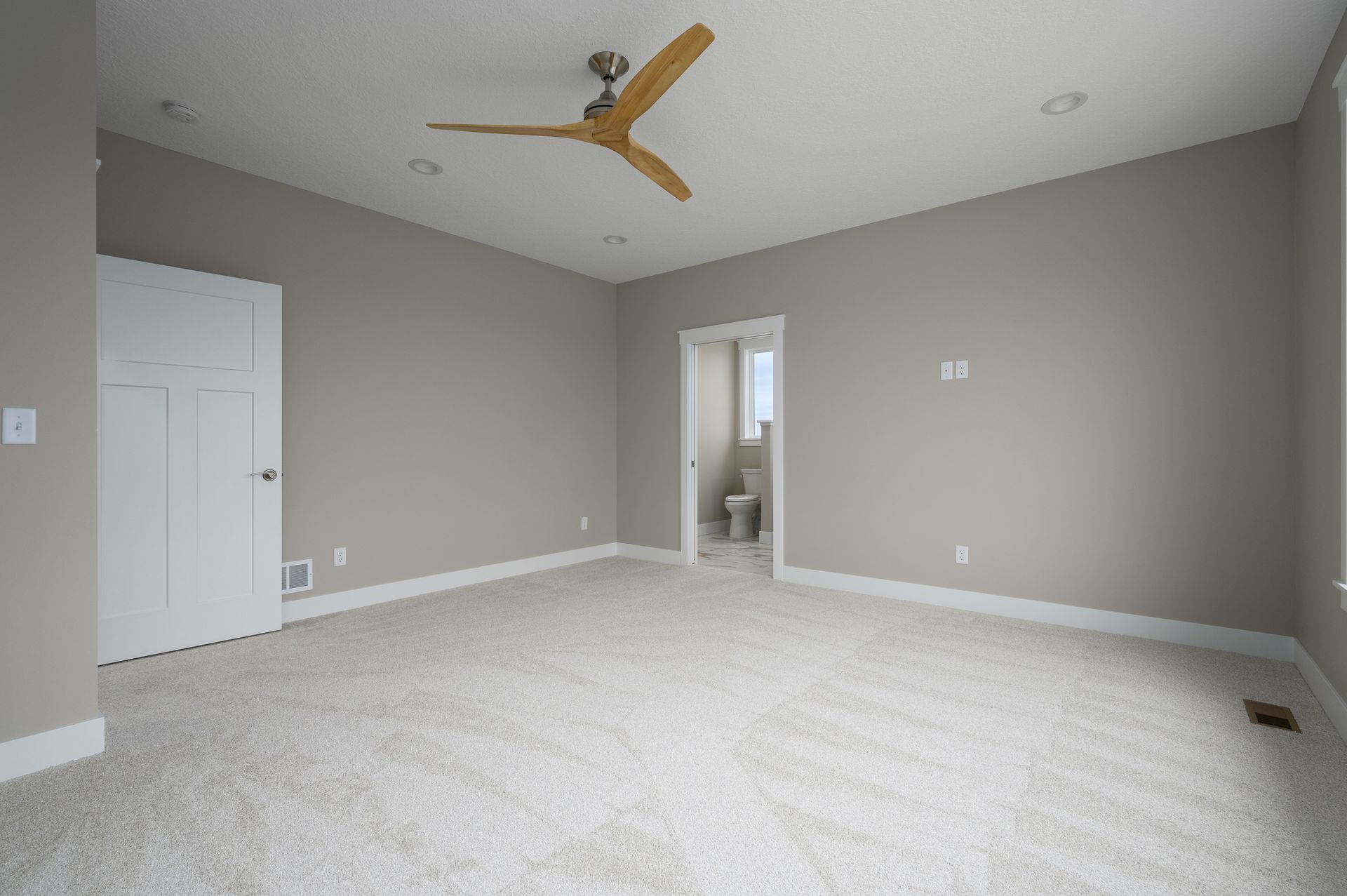 Empty room with beige walls, white trim and door, carpet flooring, and a ceiling fan.