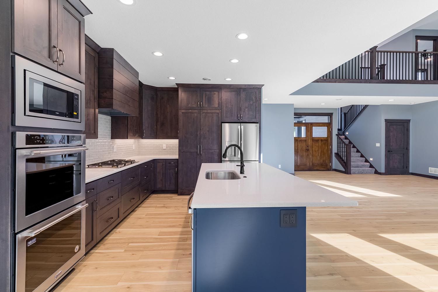 Modern kitchen with dark cabinets, stainless steel appliances, and a blue island with a white countertop.