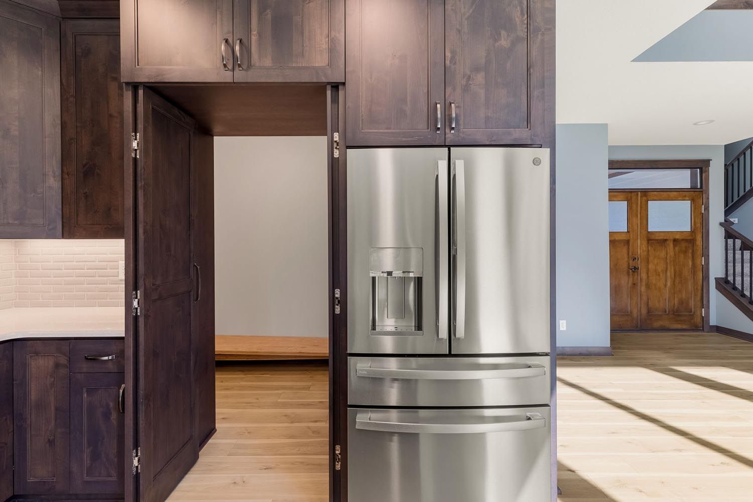Stainless steel refrigerator built into dark wood cabinetry with an open pantry.