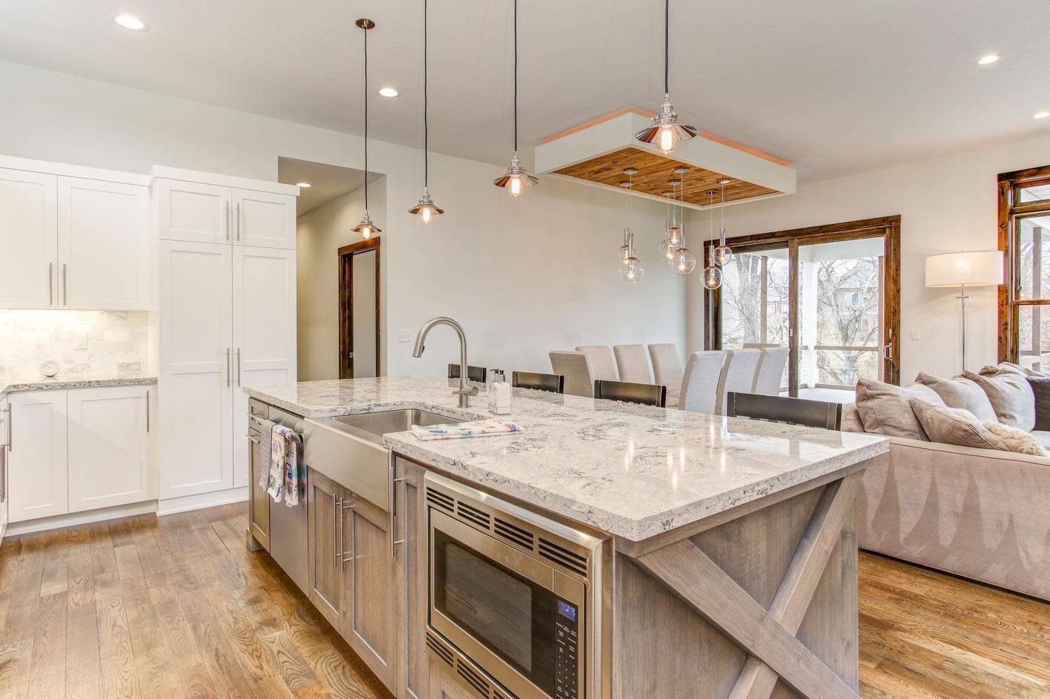 Spacious kitchen with island, sink, and microwave. White cabinets, wood floors, and large window.