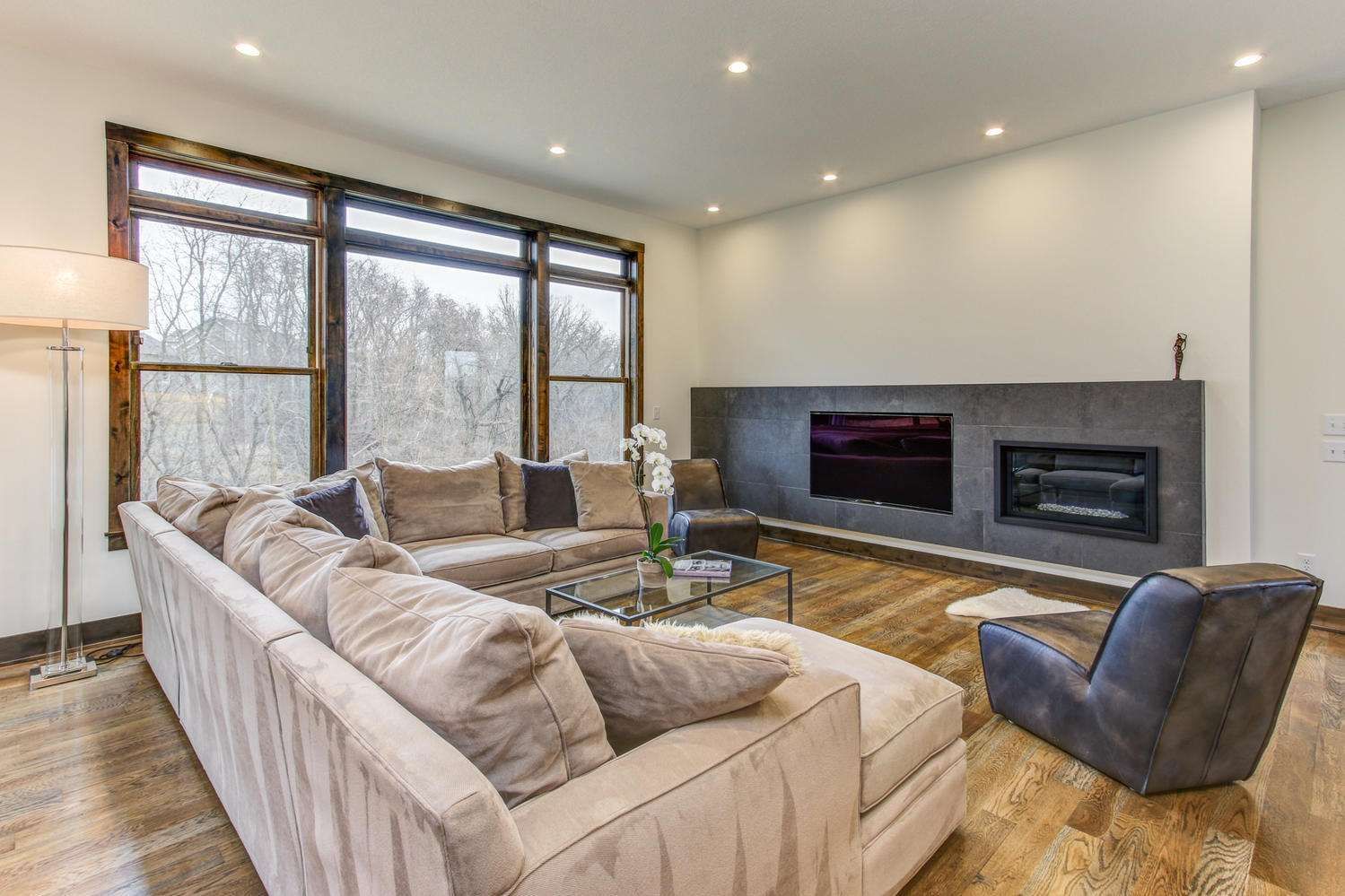 Spacious living room with sectional sofa, large windows, fireplace, and wood floors.