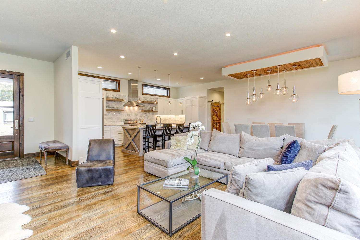 Spacious living room with open kitchen, neutral tones, wood floors, and plush seating.