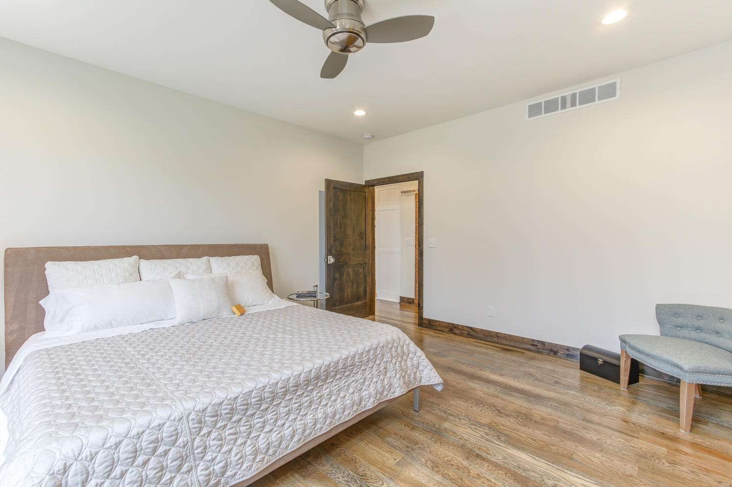 Bedroom with a large bed, hardwood floors, and a ceiling fan. A door leads to another room.