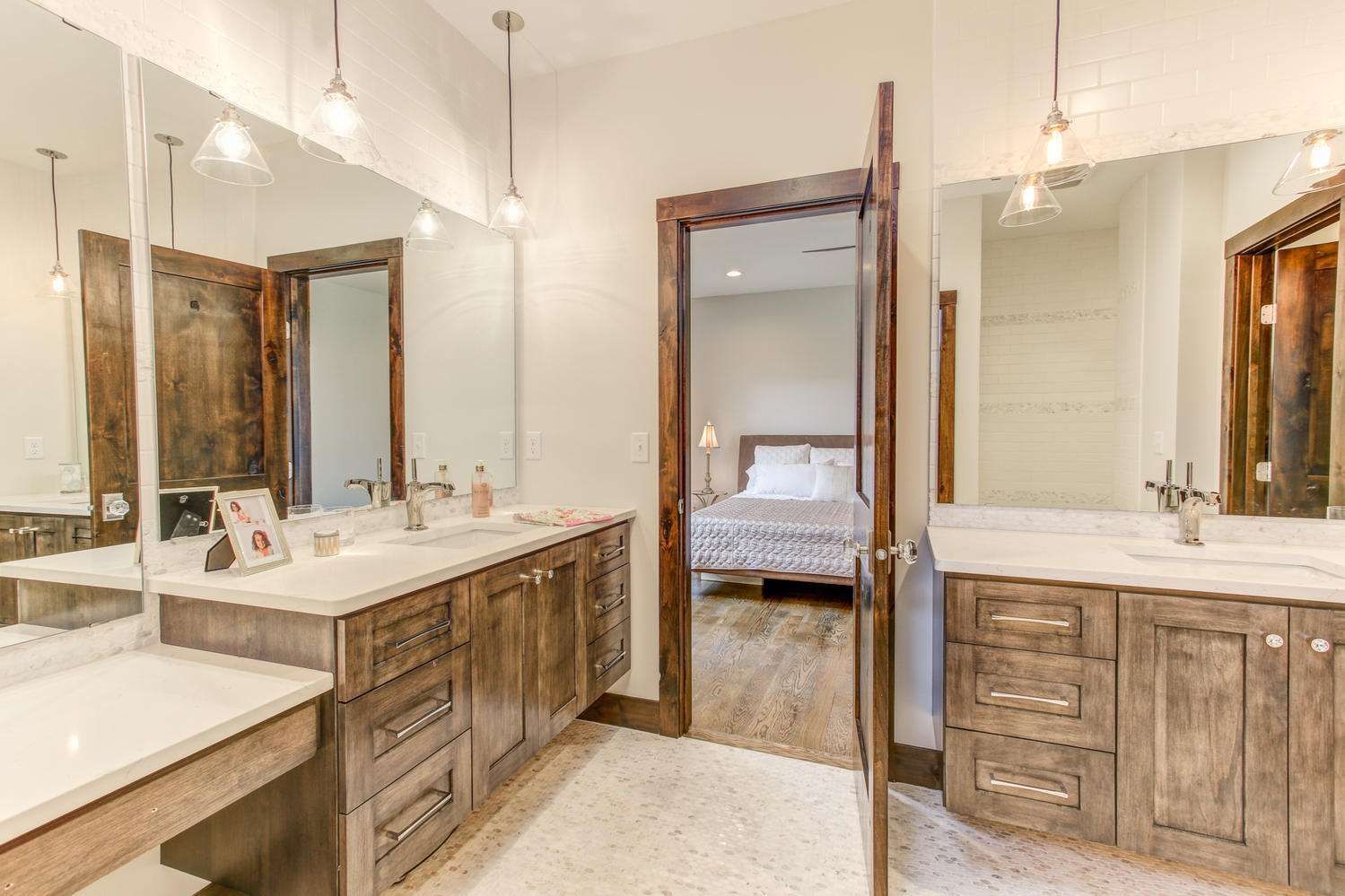 Bathroom with two vanities, open doorway to bedroom, brown wood cabinets, white countertops, large mirrors.