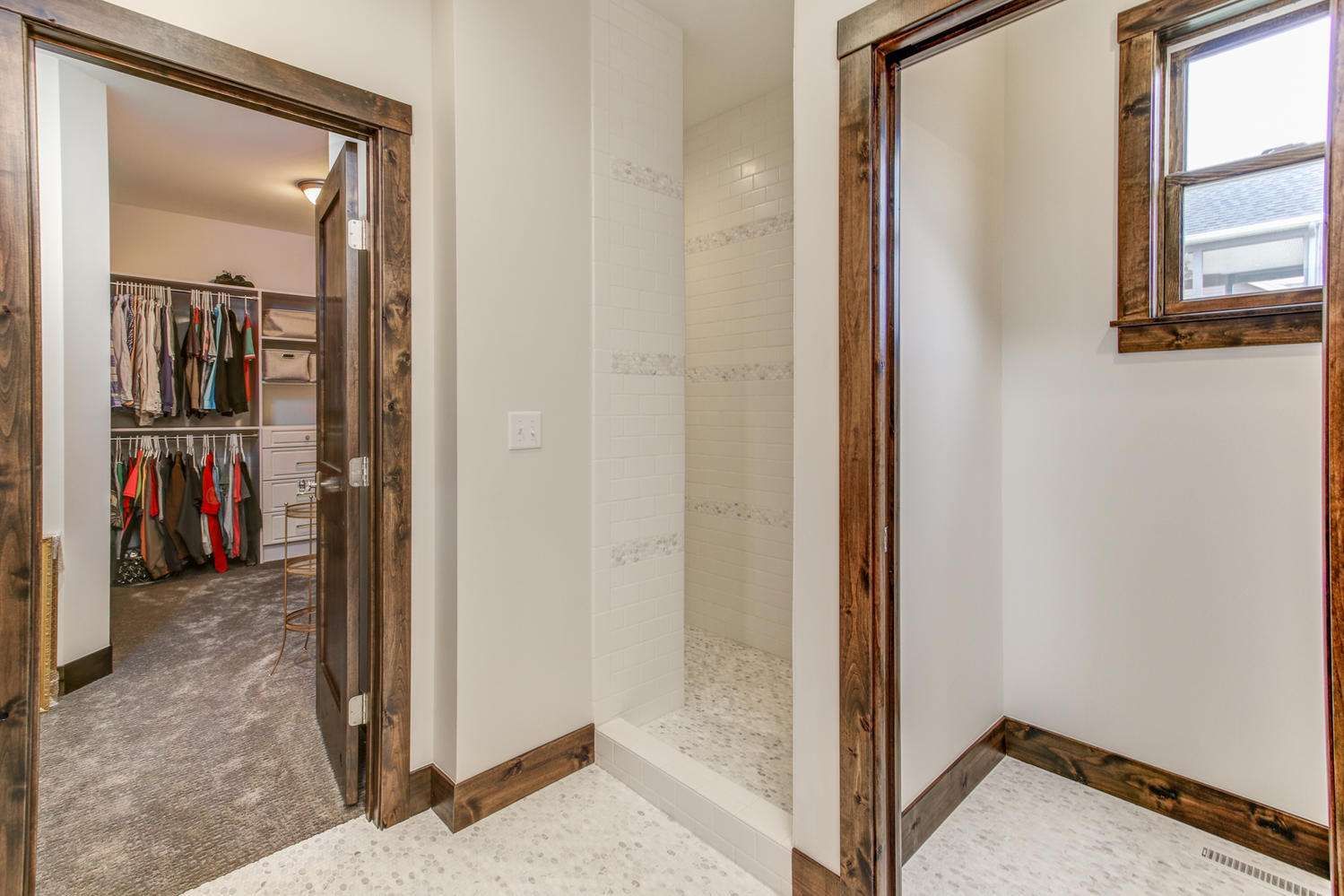 Interior view of a bathroom with a walk-in closet, shower, and window, all with wood trim.