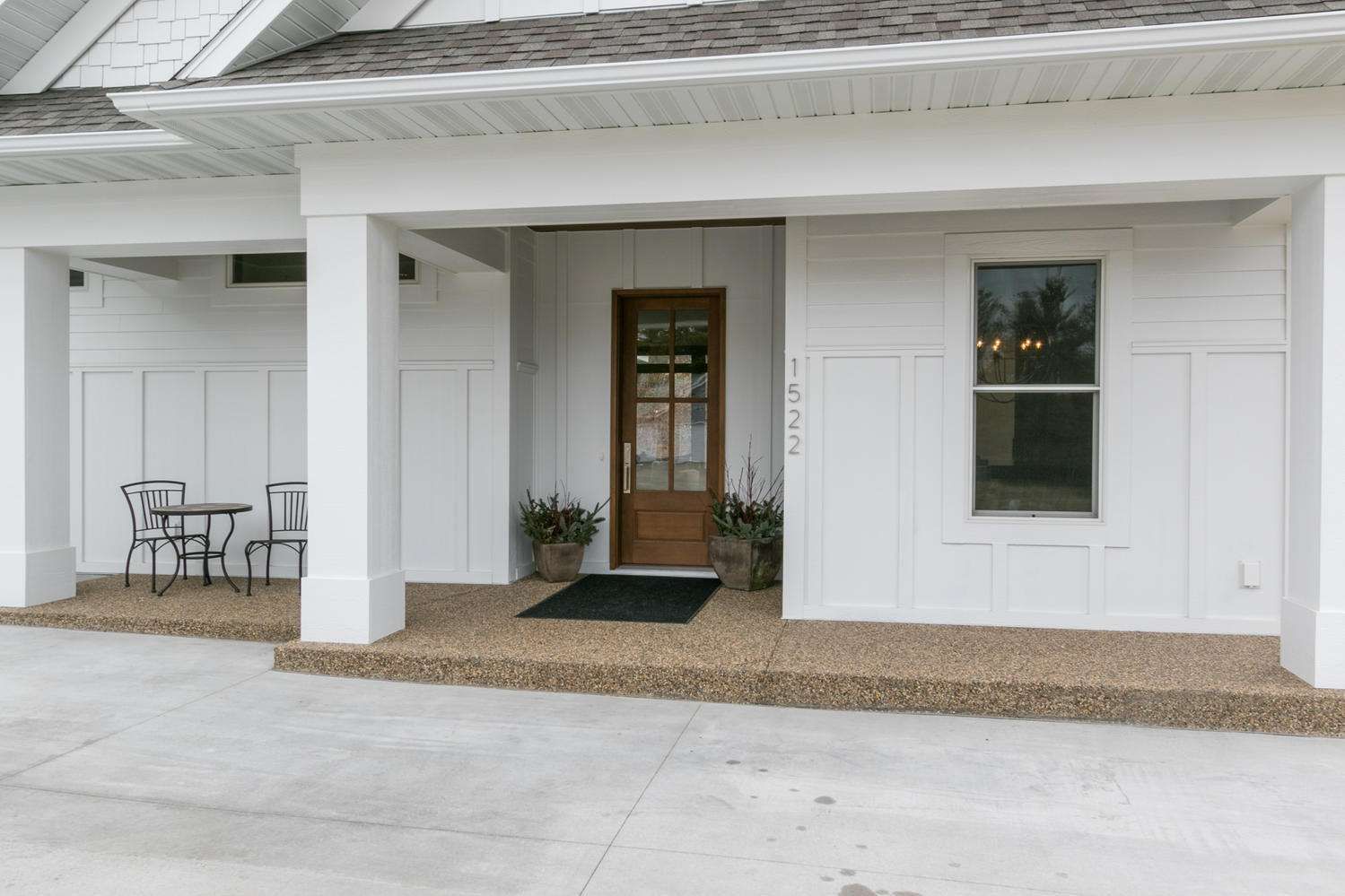 White building with a brown door, window, and gravel path. Outdoor table and chairs on left.