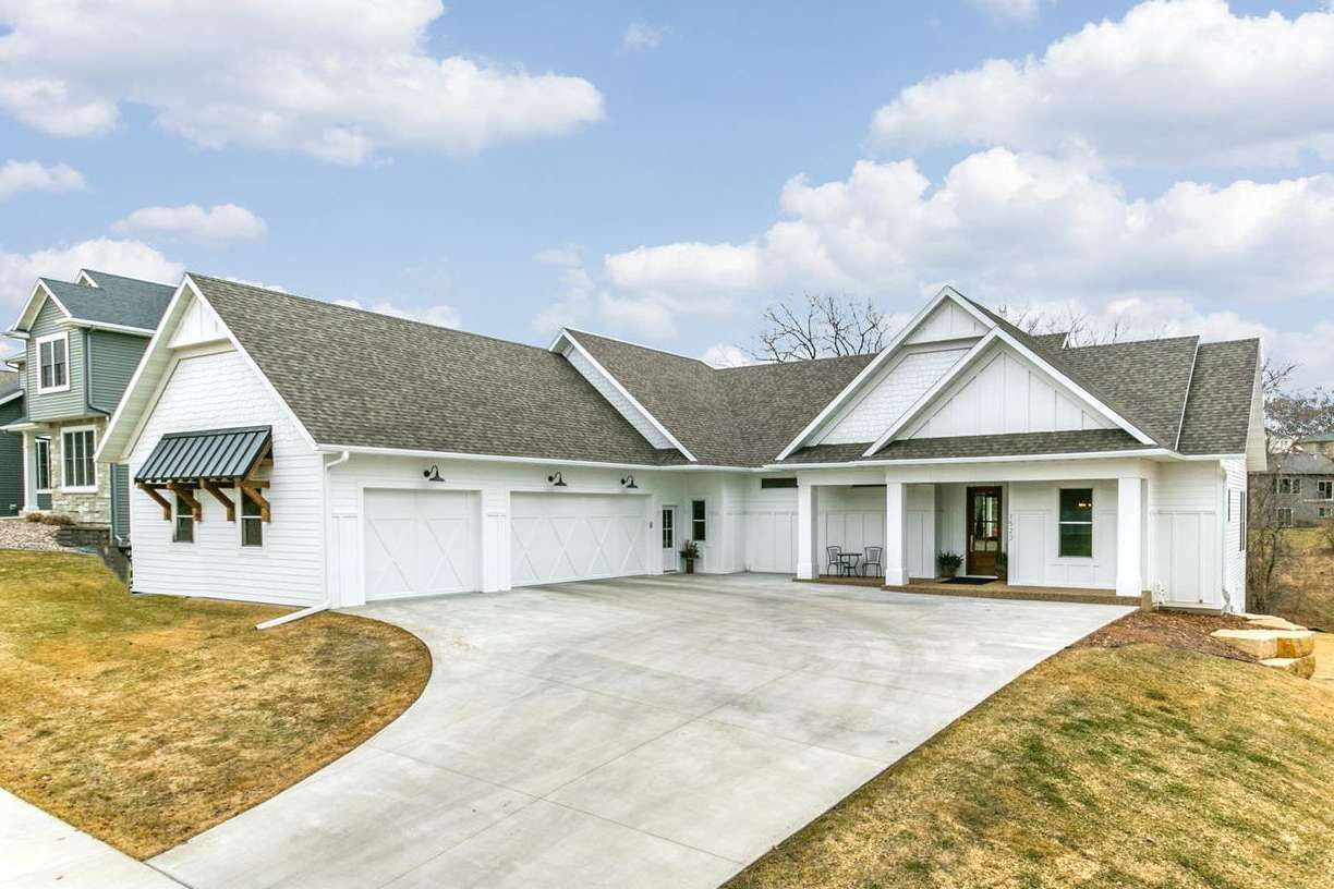 White house with a gray roof and attached two-car garage. A concrete driveway slopes towards the house under a cloudy sky.