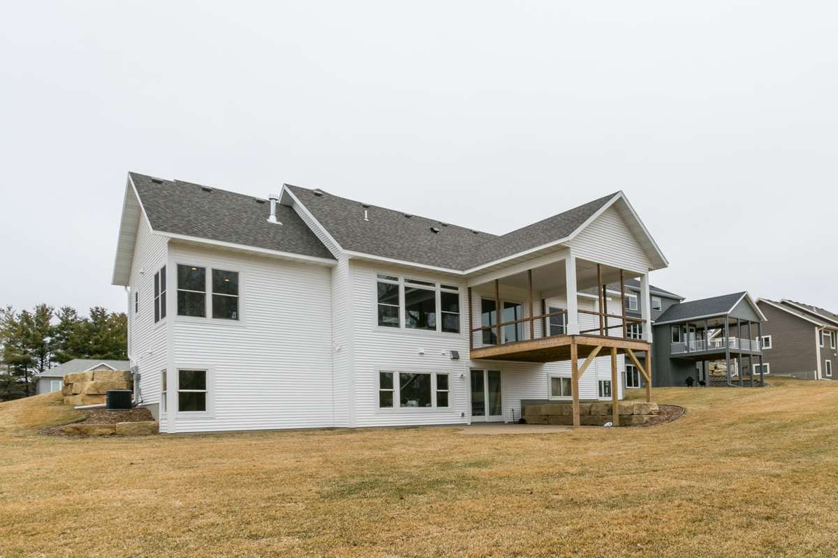 White two-story house with a screened porch and large windows on a grassy lot under a gray sky.