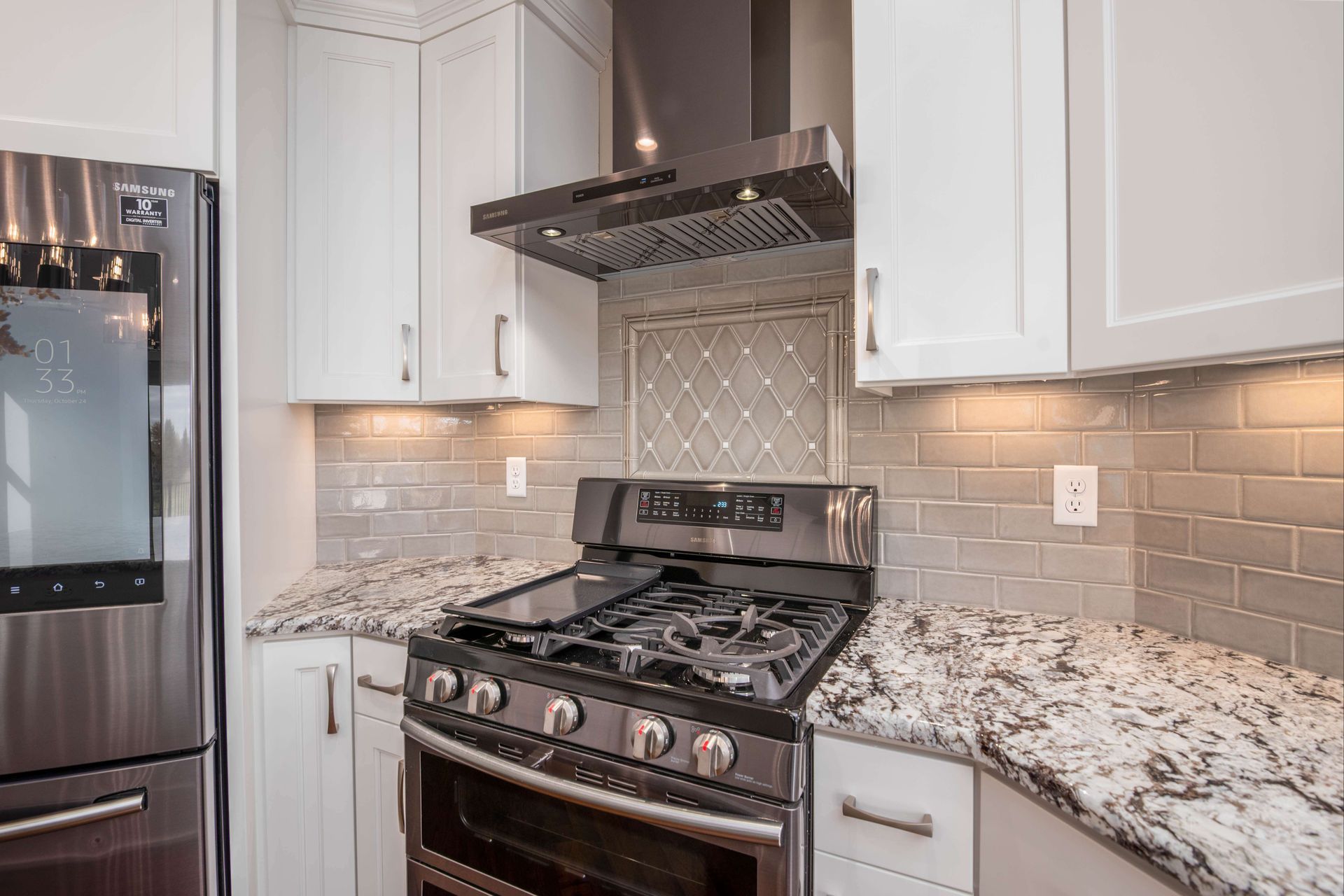 Kitchen with stainless steel appliances, white cabinets, grey backsplash, and granite countertops.