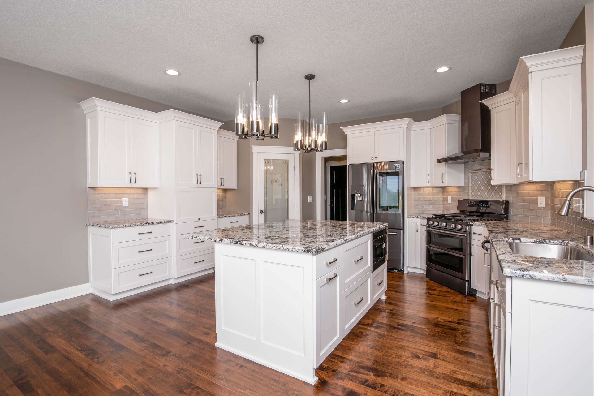 White kitchen with island, cabinets, granite countertops, and hardwood floors.
