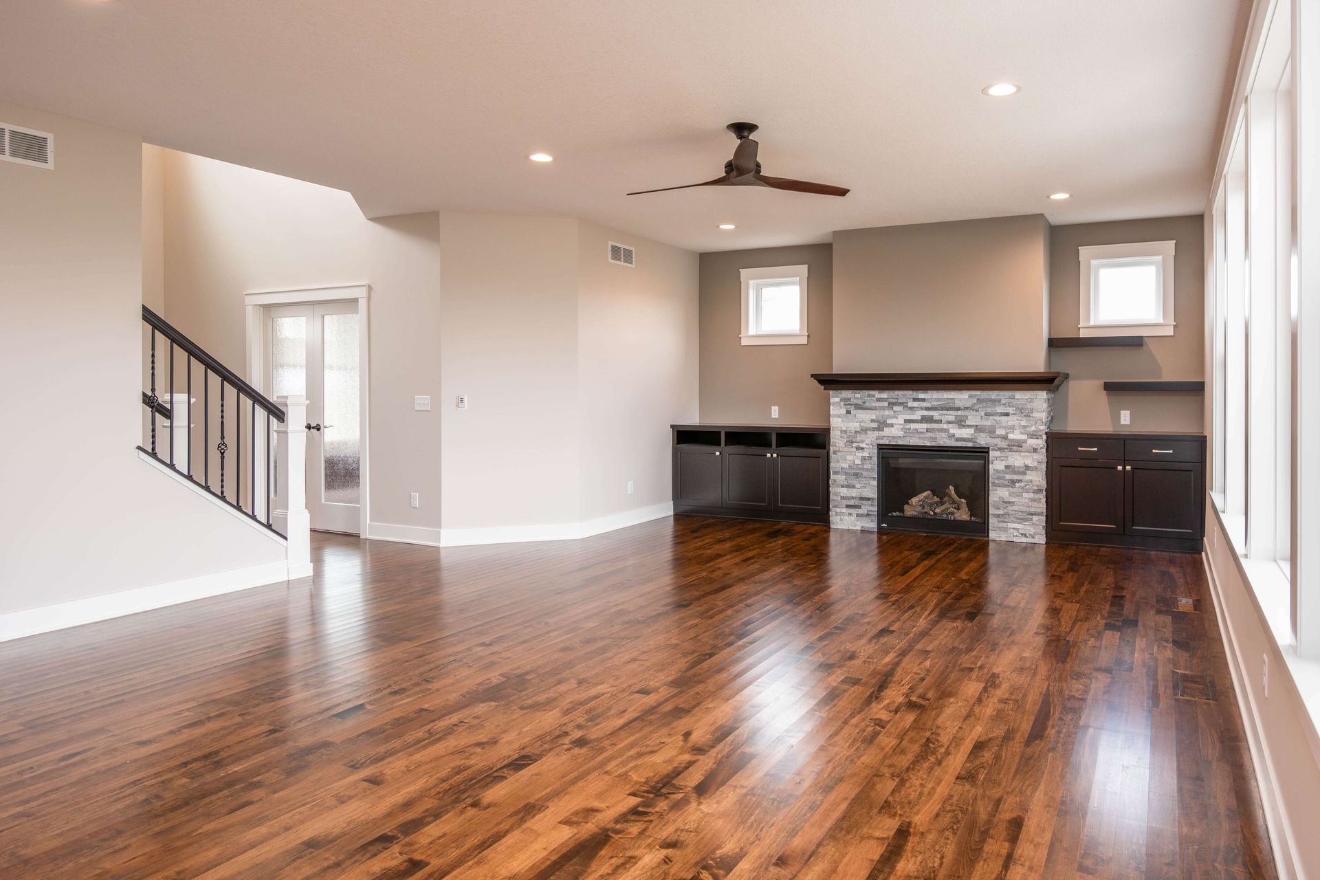 Empty living room with dark wood floors, fireplace, and staircase.