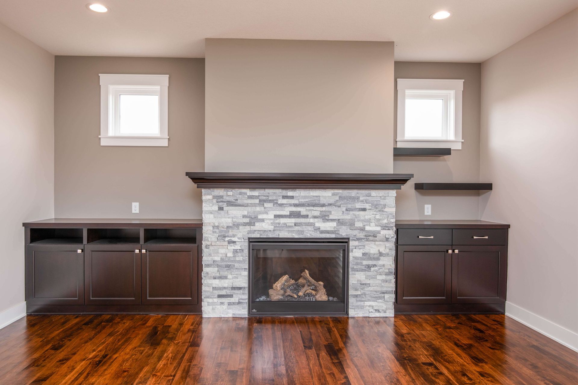 Living room with fireplace, stone facade, dark wood cabinets, and dark wood floor.