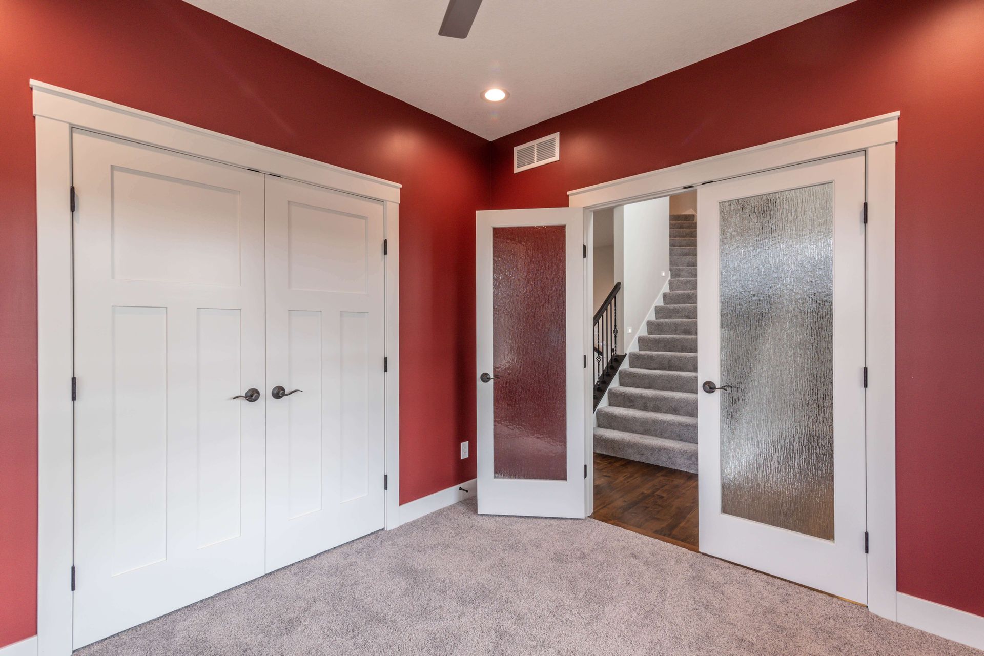 Red-walled room with white doors: two solid doors, two frosted glass doors leading to a staircase, carpeted floor.