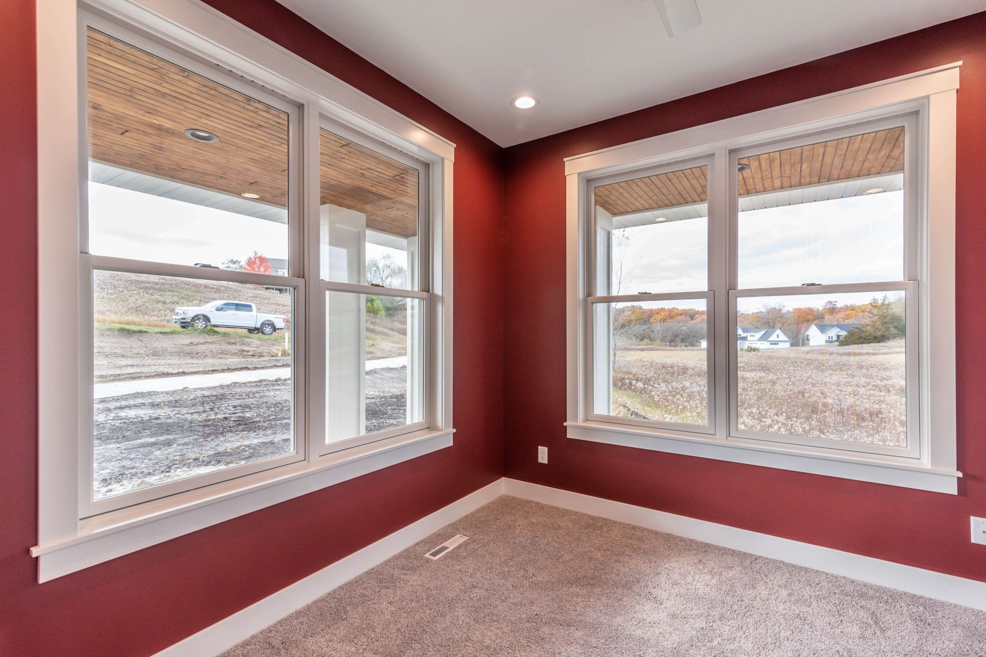 Corner room with two windows, red walls, white trim, and a beige carpet.