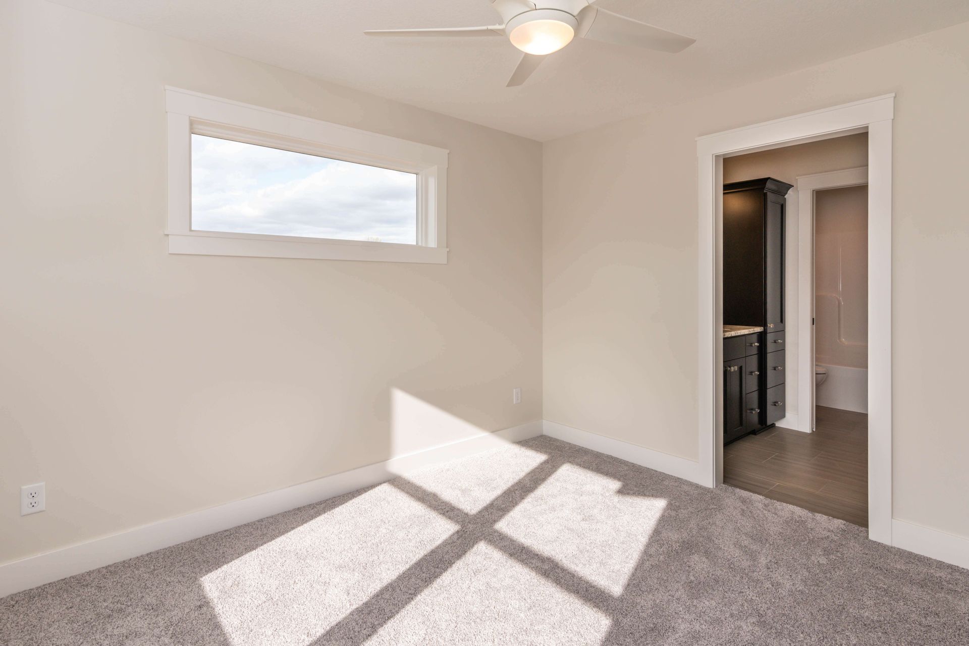 Empty bedroom with window, ceiling fan, and open doorway leading to a bathroom.