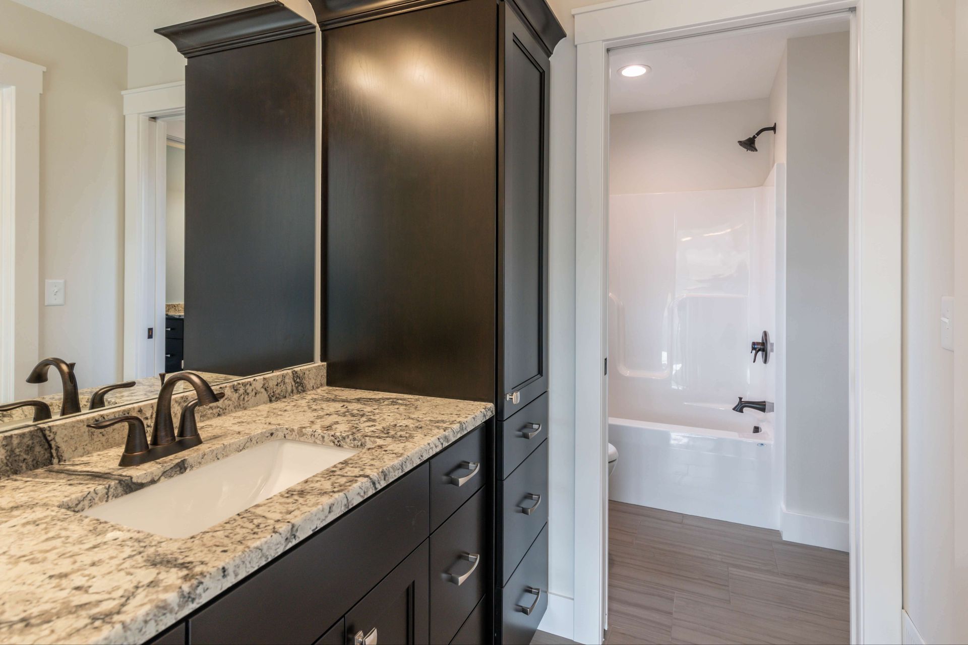 Bathroom with dark cabinets, granite countertop, white sink, and shower in the background.