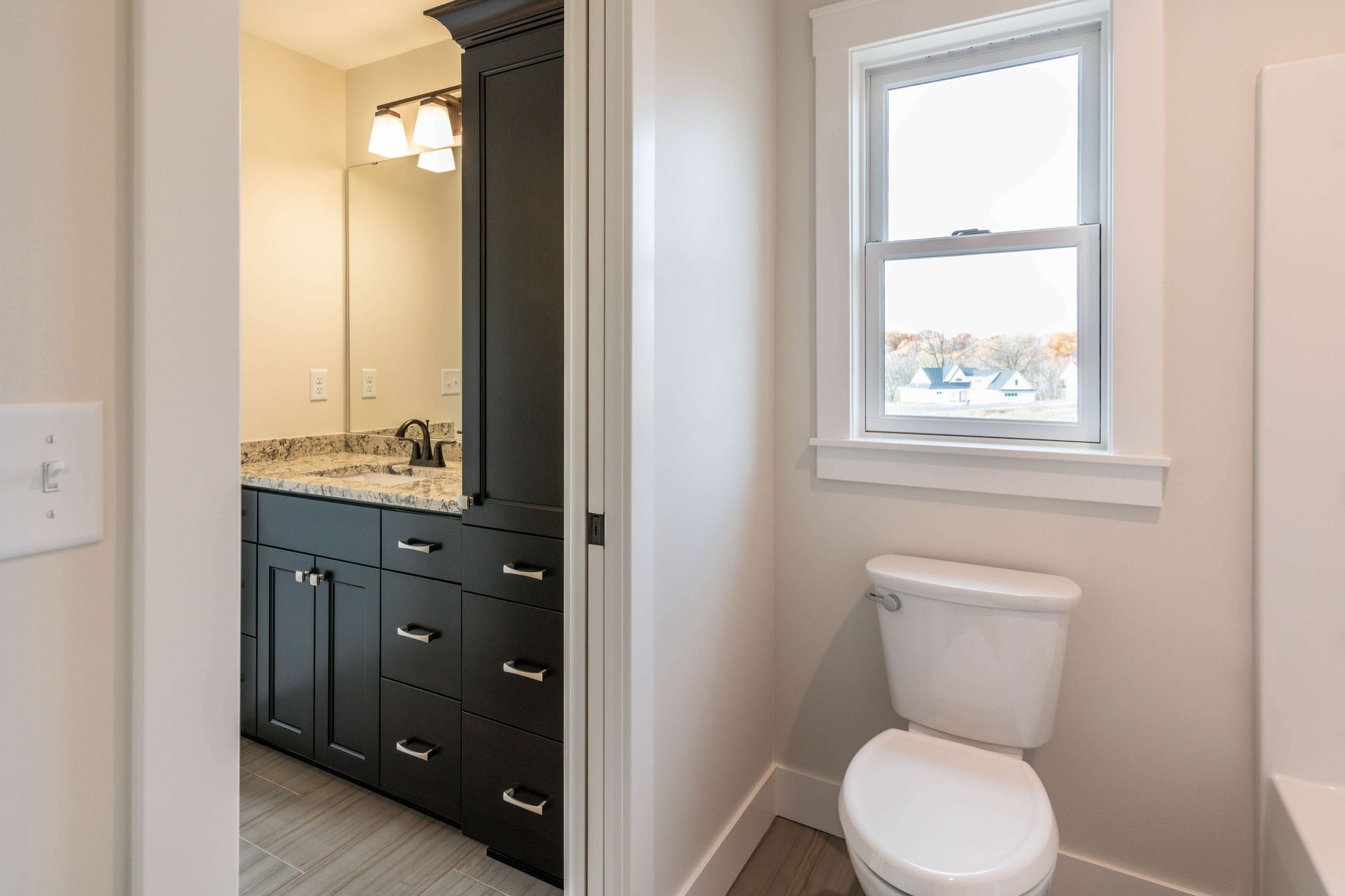 Bathroom interior with dark vanity, white toilet, and window.