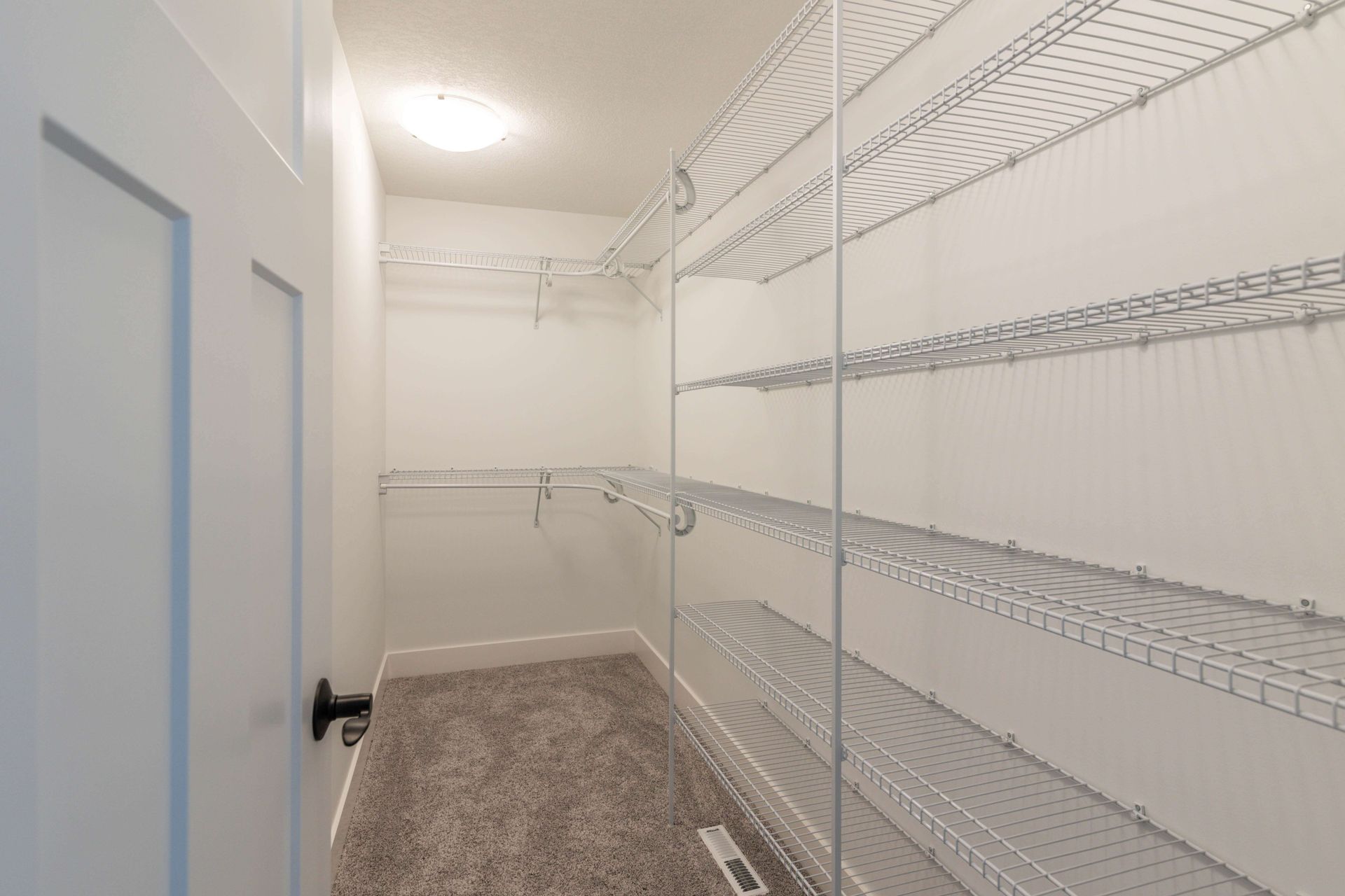 Empty white walk-in closet with wire shelving and a closed door. Light carpet on the floor.