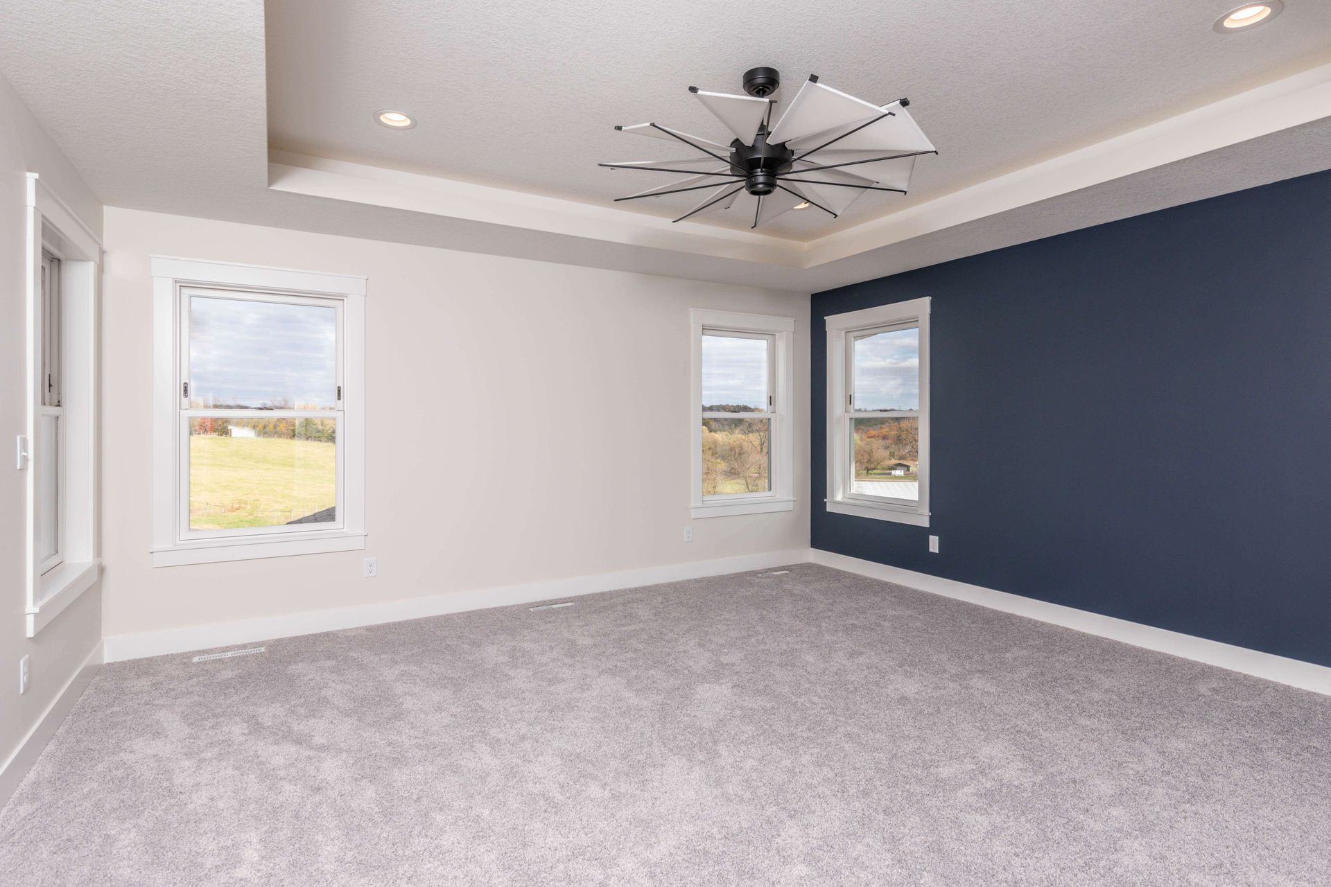 Empty bedroom with blue accent wall, white walls, and gray carpet.