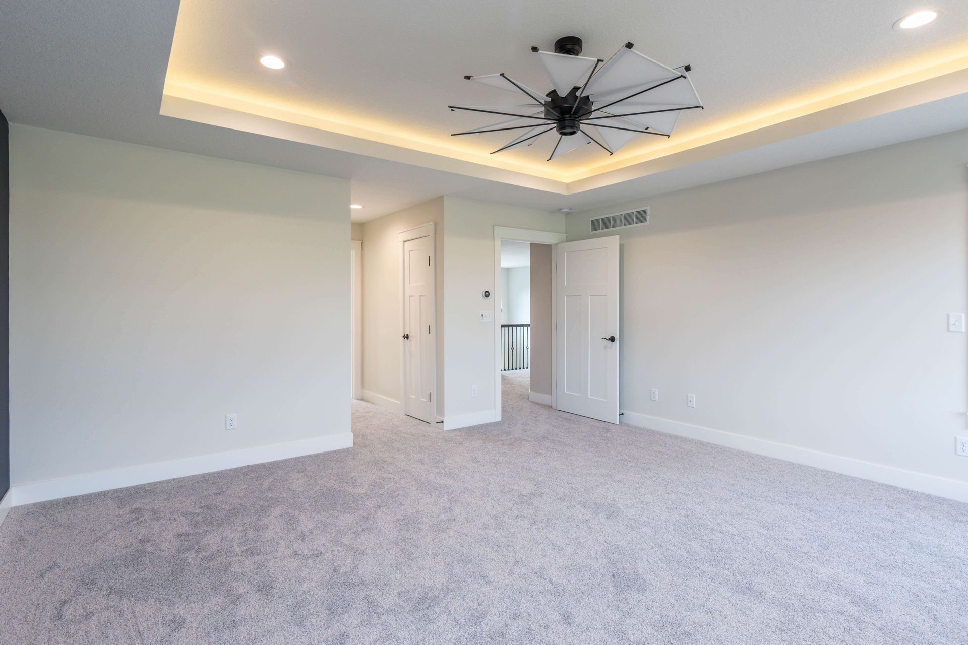 Empty bedroom with gray carpet, white walls, and a decorative ceiling light.