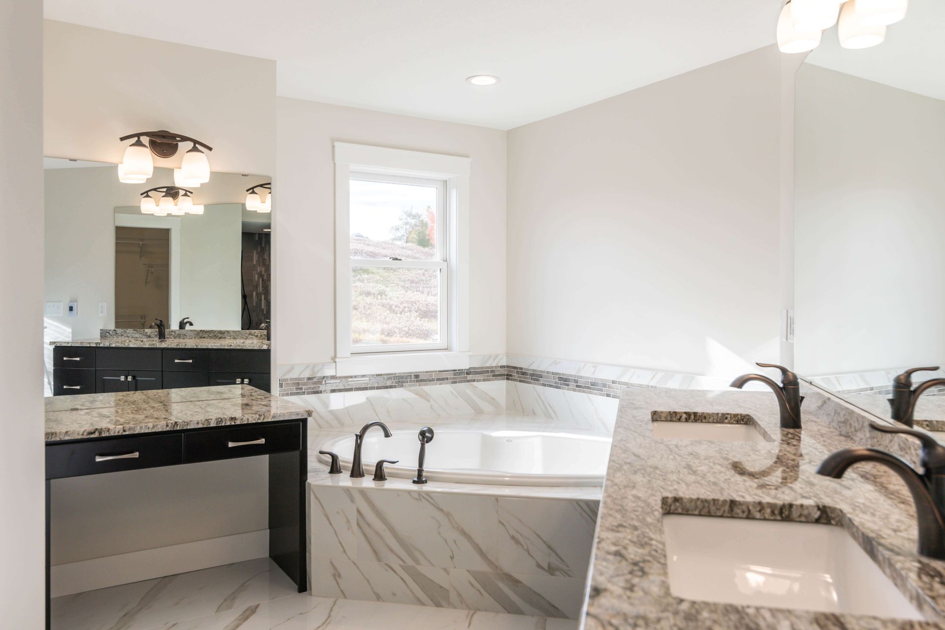 Modern bathroom with tub, double sink, marble countertops, and vanity.