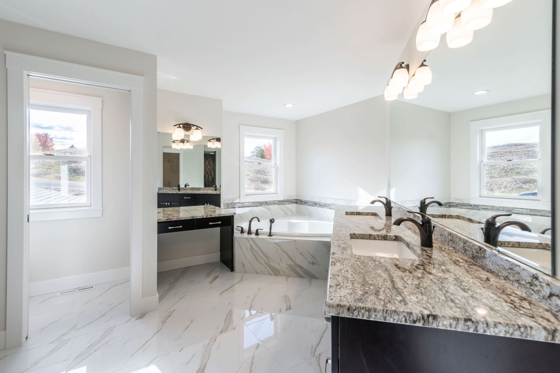 Bright white bathroom with marble floors, a soaking tub, and dual sinks with granite countertops.