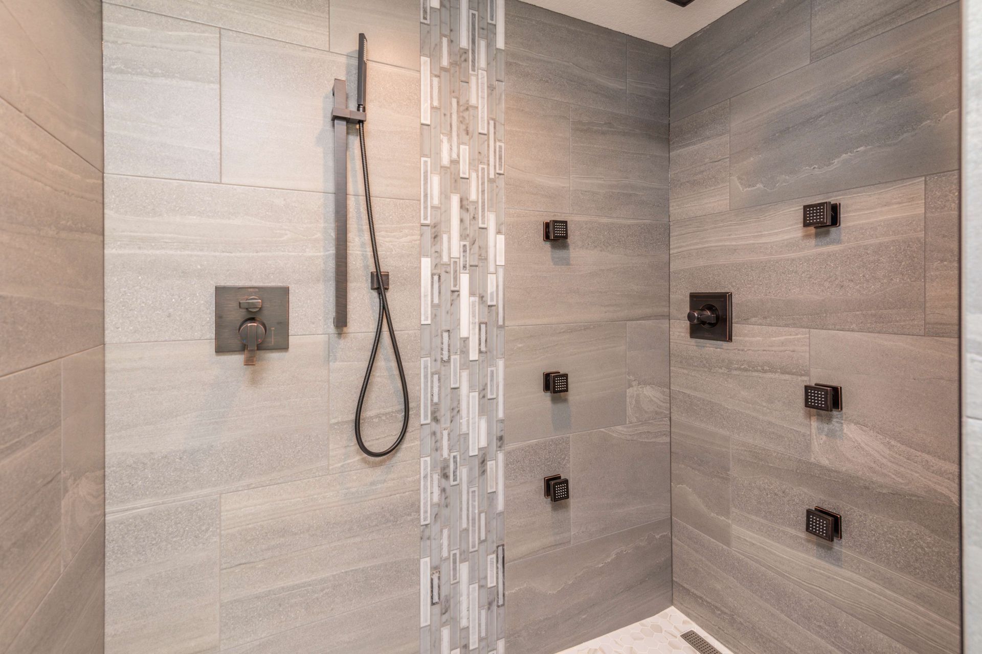Modern shower with gray tiled walls, multiple shower heads, and a handheld shower.
