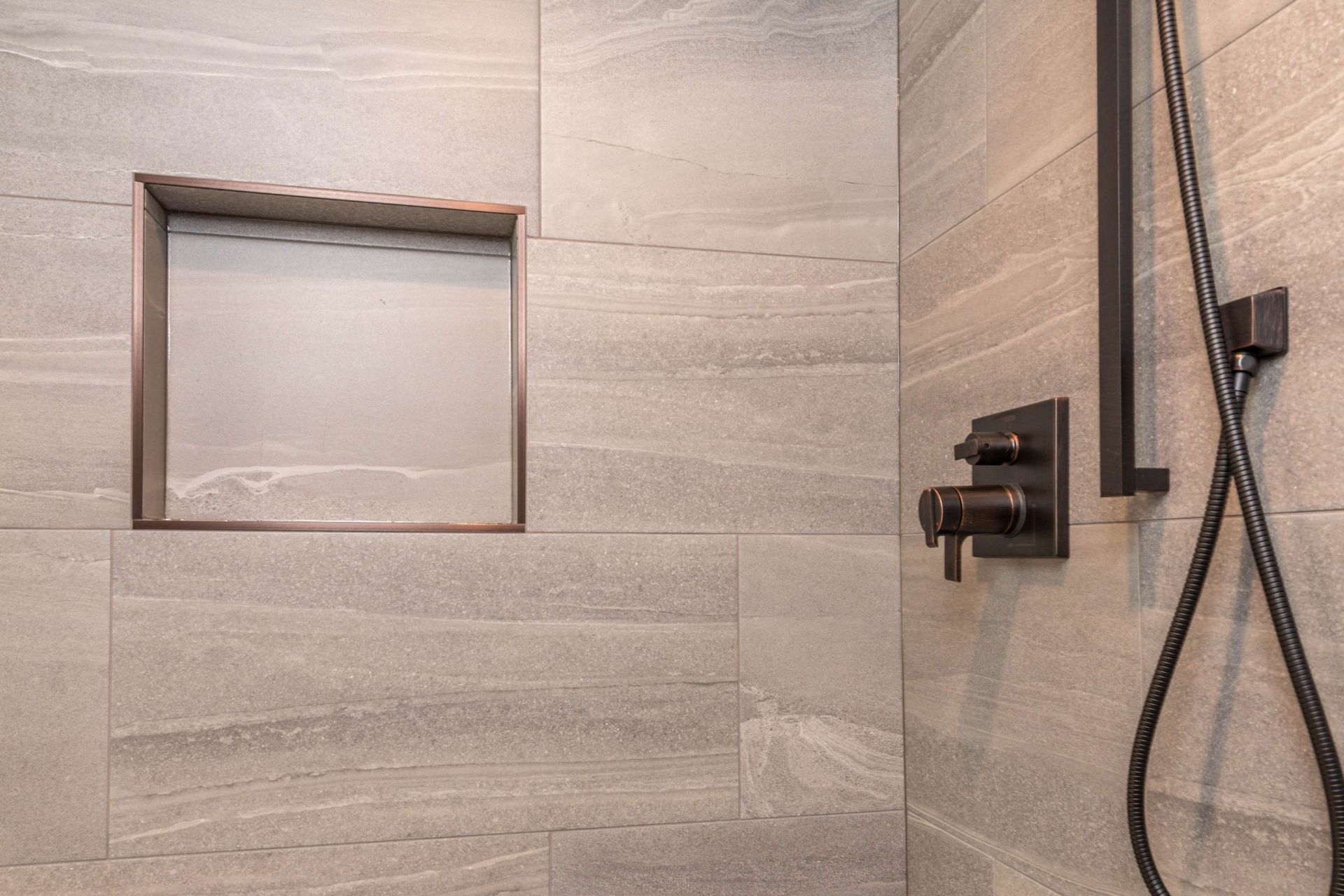 Shower stall with gray textured tile, recessed shelf, and black fixtures.