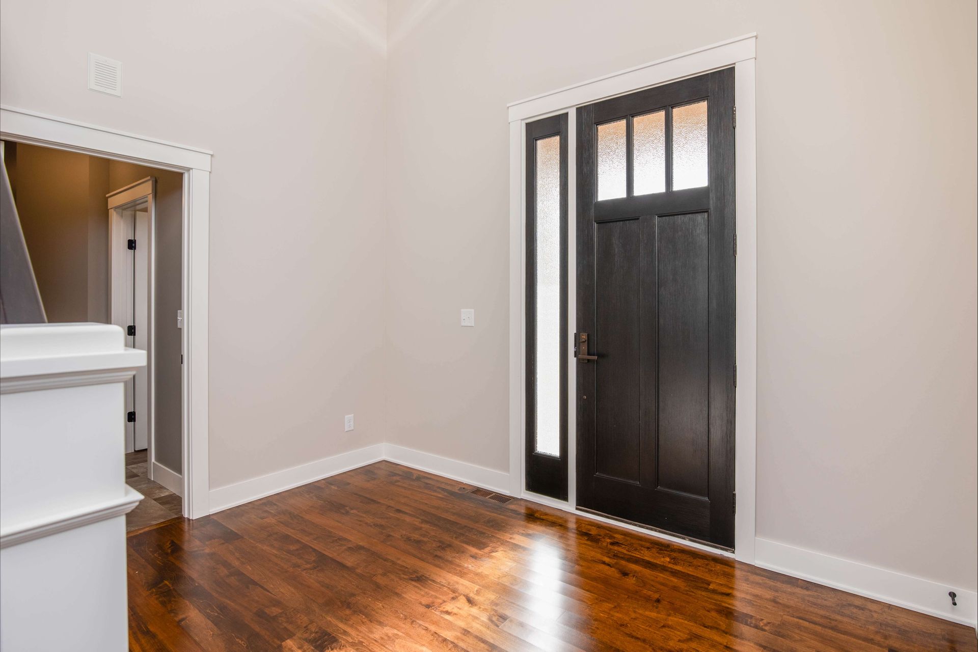 Interior of a home with a black front door, sidelight, and wood floors.