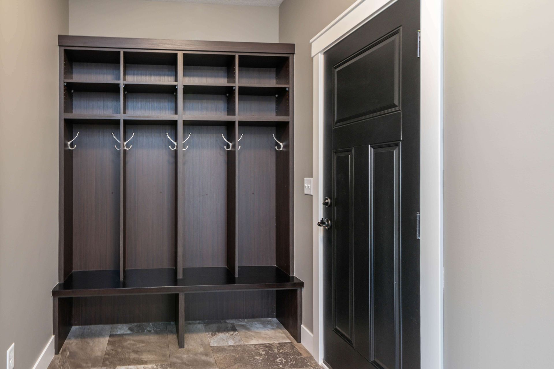 Dark wooden entryway storage unit with cubbies, hooks, and bench next to a black door.