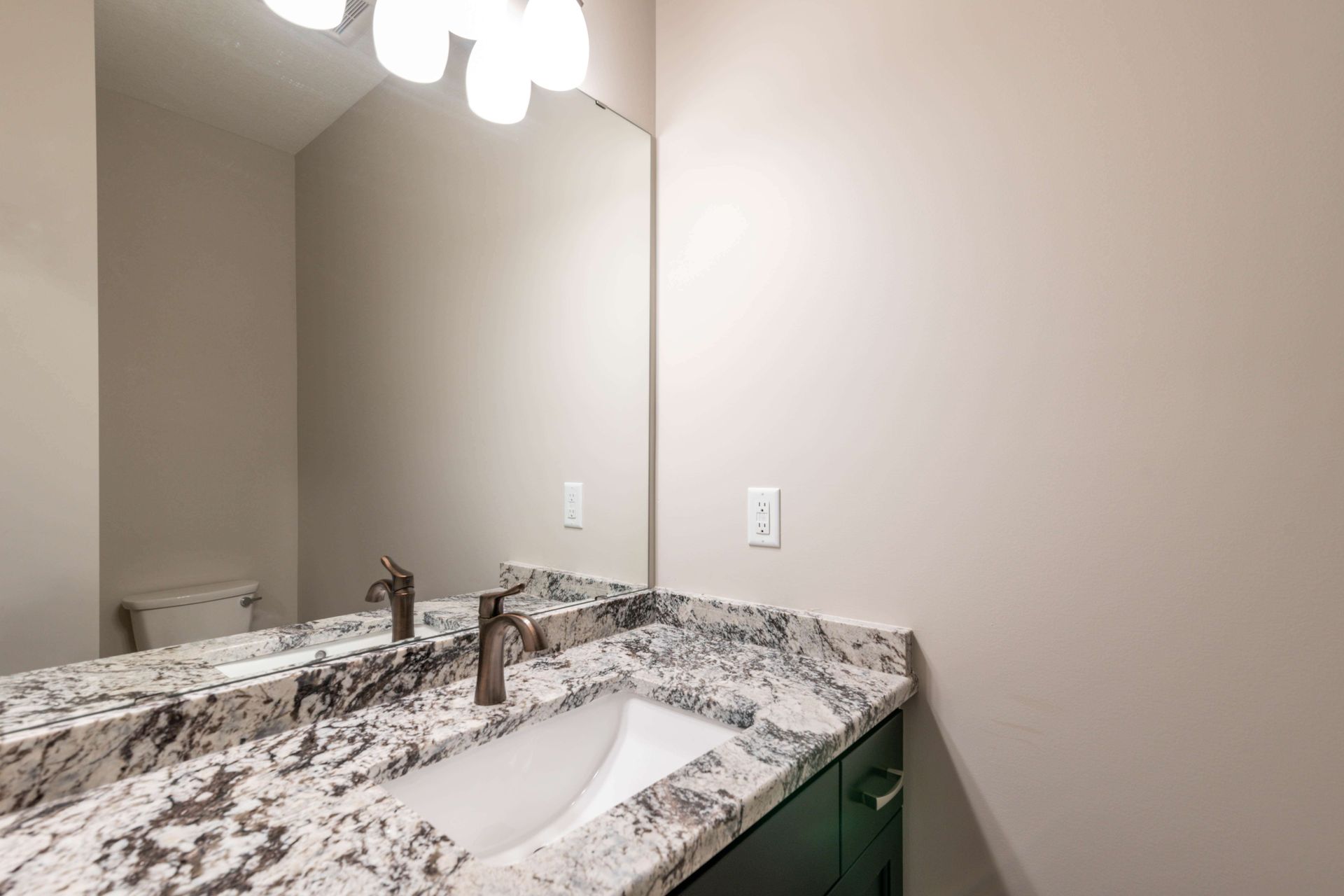 Bathroom with white sink, granite countertop, large mirror, and beige walls.