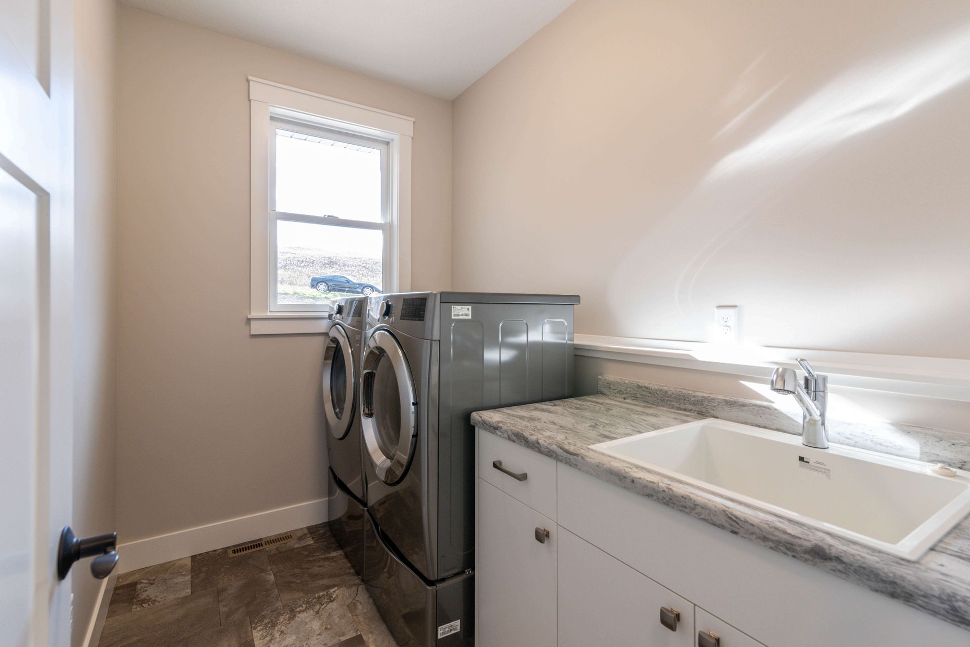Laundry room with gray washer/dryer, white cabinets, and a sink beneath a small window.
