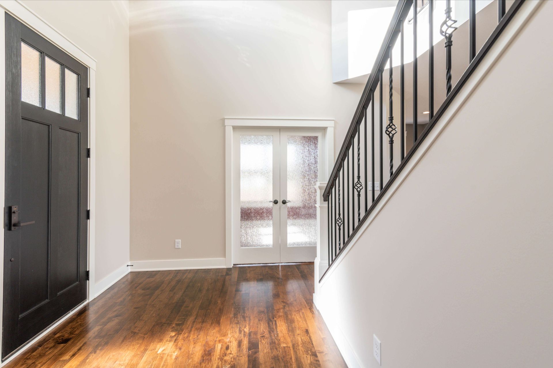 Entryway with a black door, wood floor, stairs with black railing, and double glass doors.