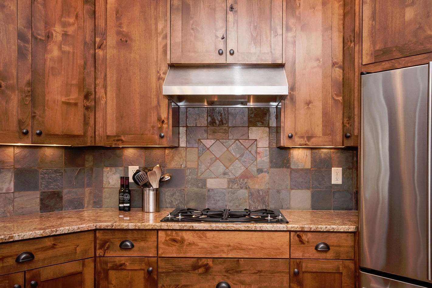 Kitchen with wood cabinets, stone backsplash, and stainless steel appliances.