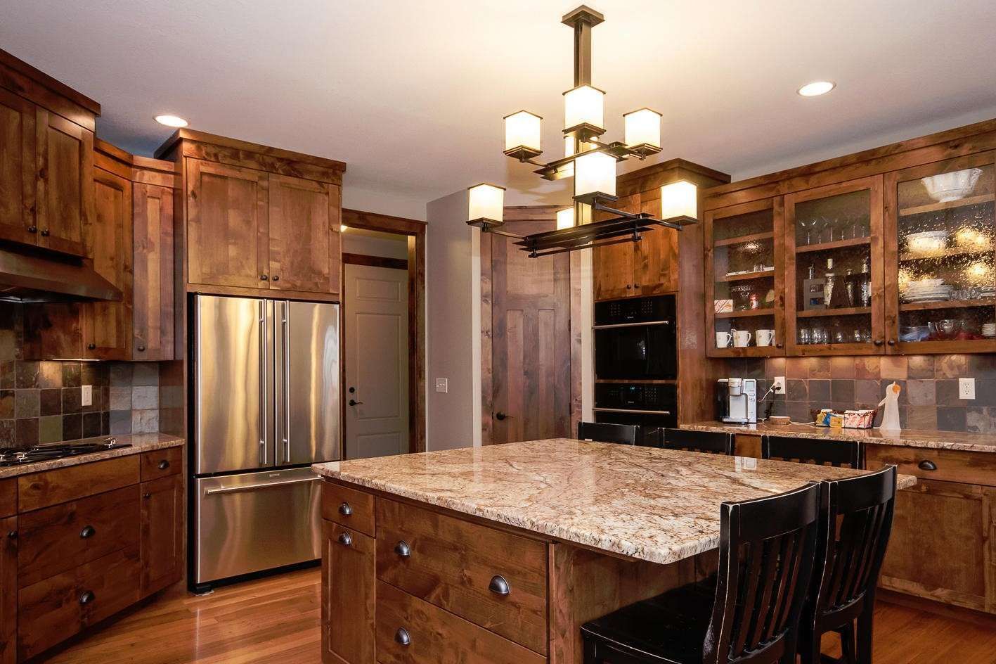 Kitchen with wood cabinets, island, stainless steel refrigerator, and modern chandelier.