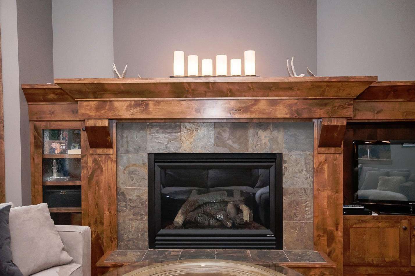 Fireplace with stone tile surround, wooden mantel, built-in cabinets, candles, and a television.