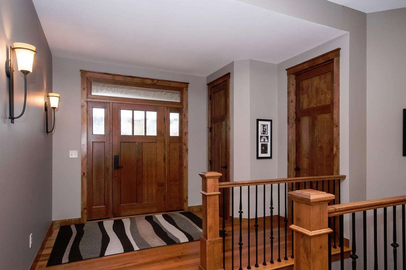 Wooden entryway with steps, front door, and adjacent wall sconces.