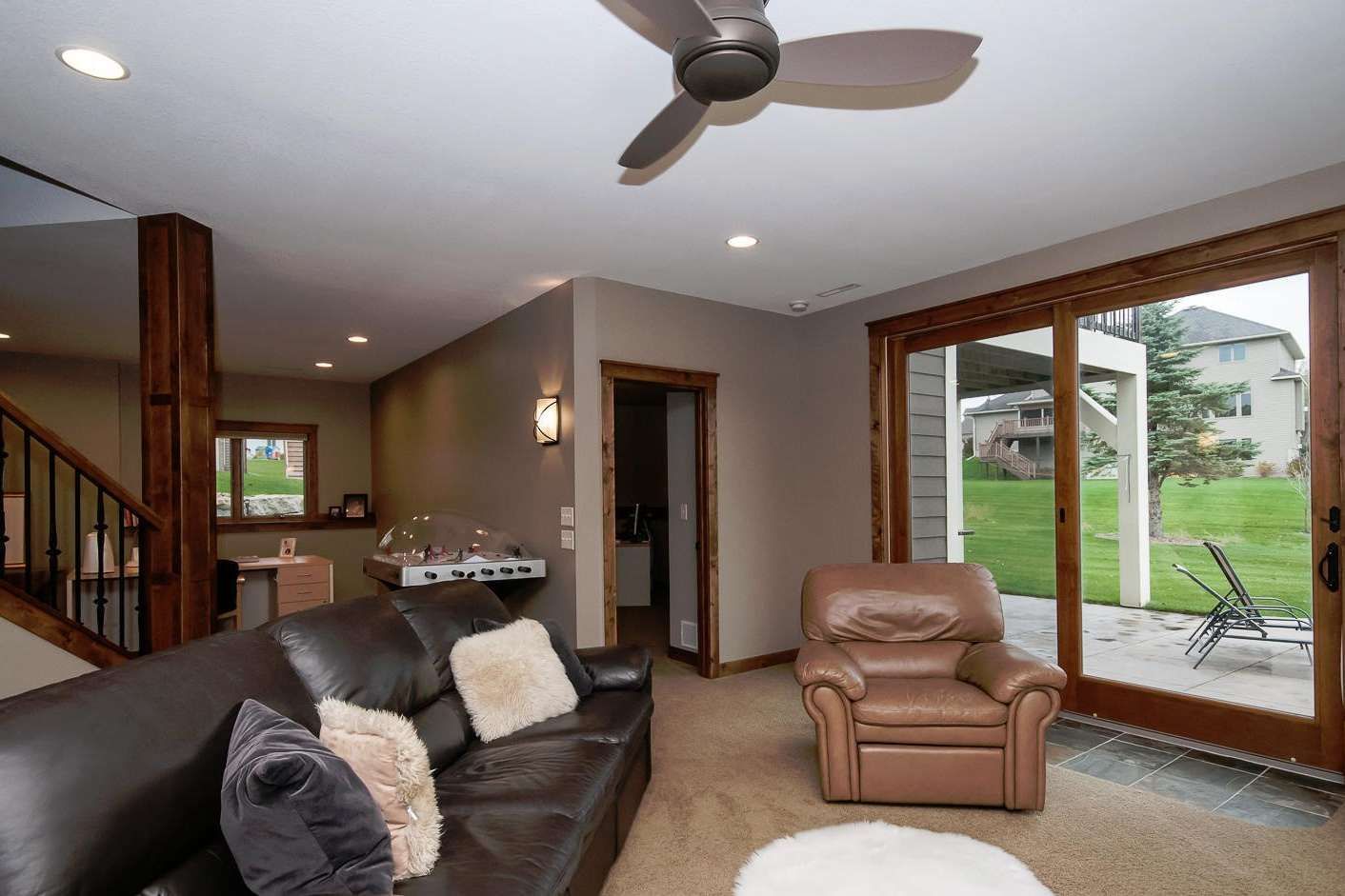 Living room with brown leather sofa, recliner, sliding door to patio, and ceiling fan.
