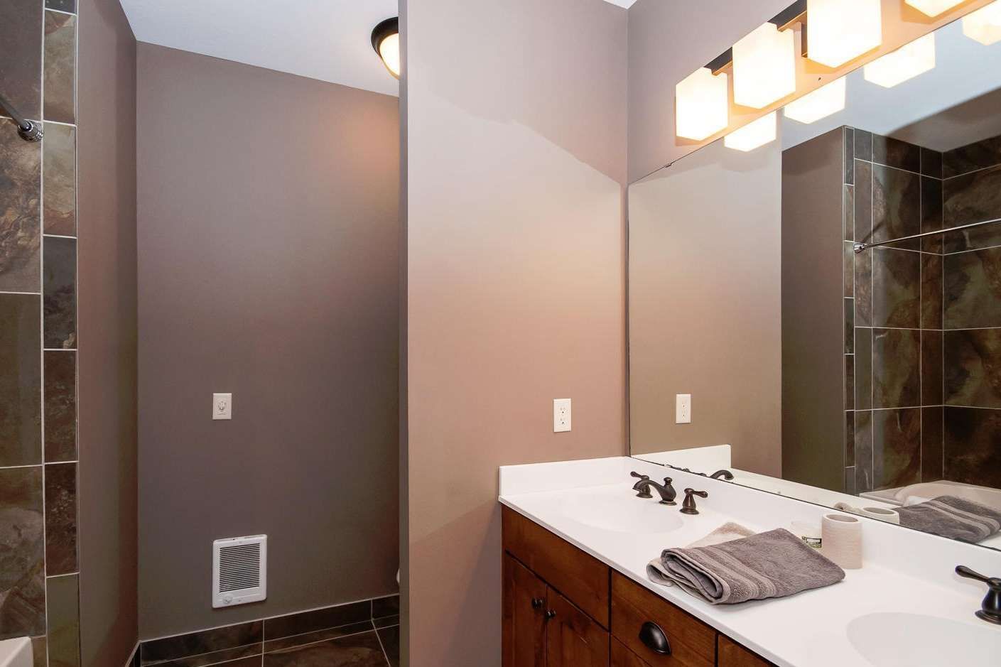 Bathroom with double vanity, mirror, shower, and brown walls.
