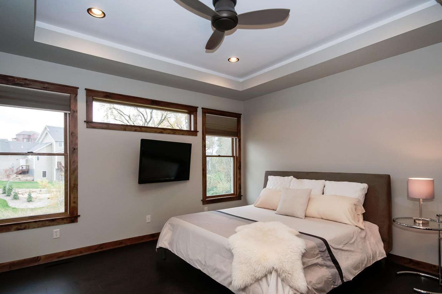 Bedroom with dark wood floors, gray walls, bed, windows, and ceiling fan.