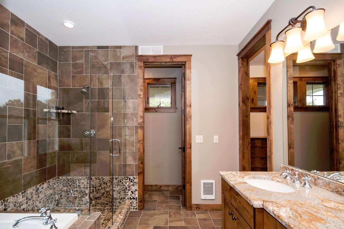 Bathroom with brown tile, wood trim, granite countertop, and glass shower.