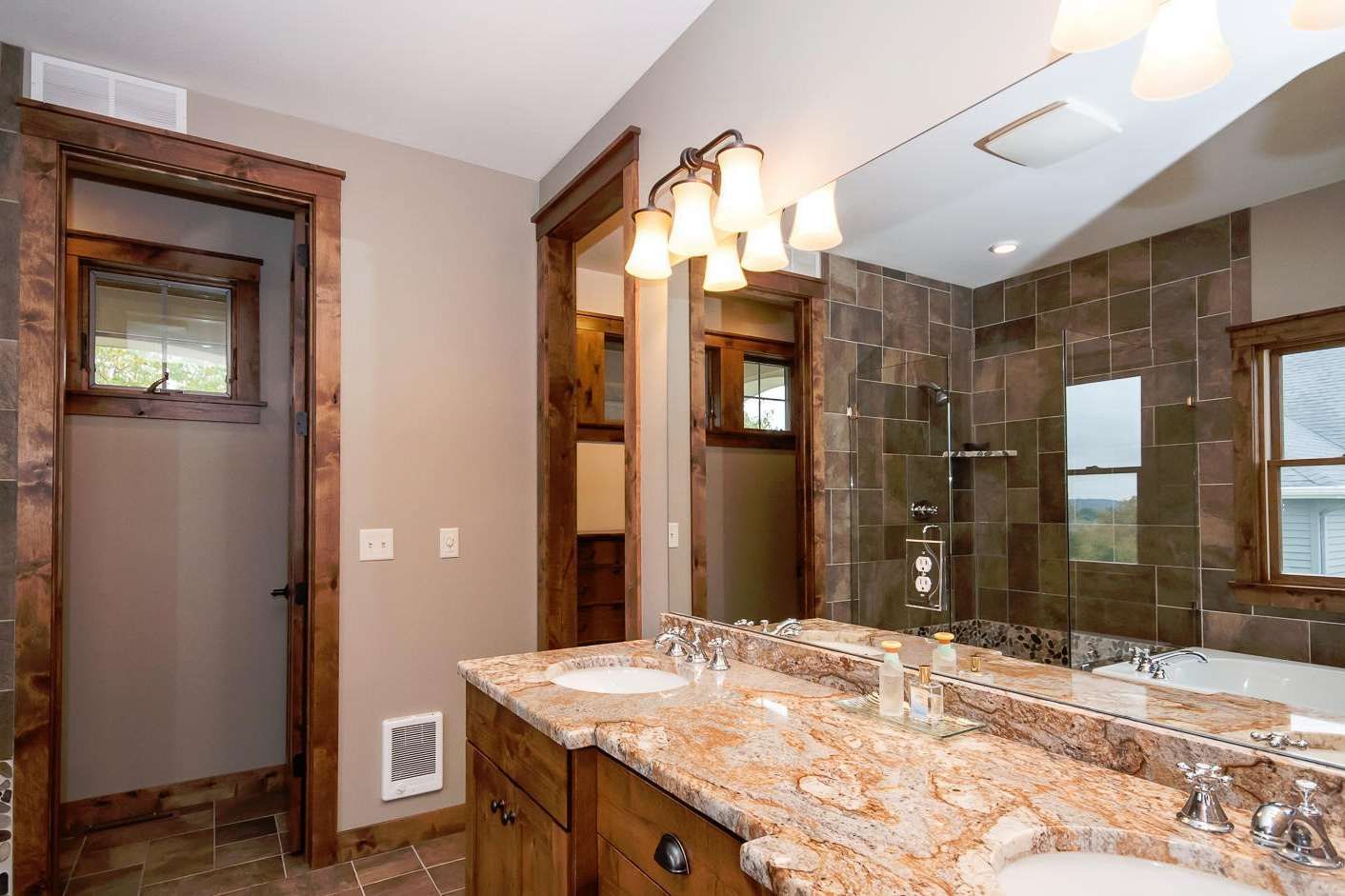 Bathroom with brown wood trim, granite countertop with two sinks, and stone tile shower.