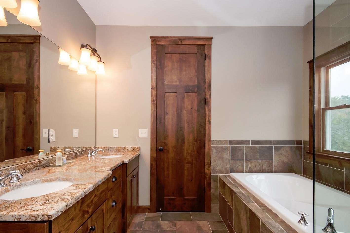 Bathroom with wood vanity, tub, and door. Tan walls, brown trim and tile.