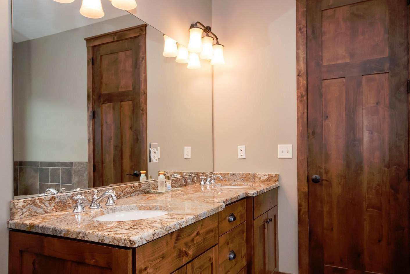 Bathroom with double vanity, granite countertop, wooden cabinets, and large mirror.